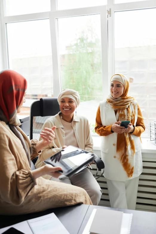 a group of women sitting next to each other in a room, a picture, shutterstock, hurufiyya, talking, white hijab, in an office, three women