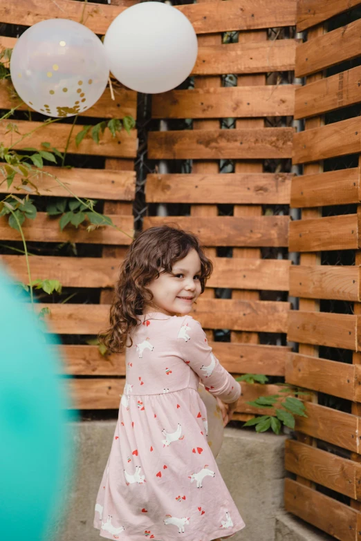 a little girl standing in front of a bunch of balloons, wooden fence, high-quality photo, portrait image, trending photo