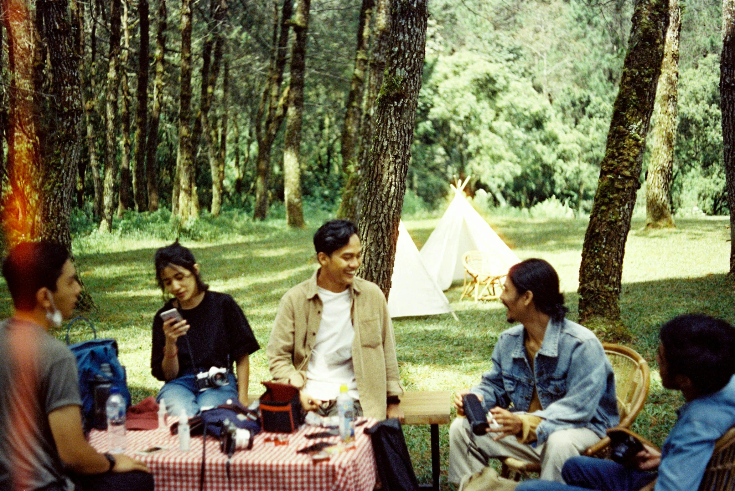 a group of people sitting around a table in the woods, a picture, flickr, sumatraism, 90's photo, glamping, photo taken on fujifilm superia, handsome