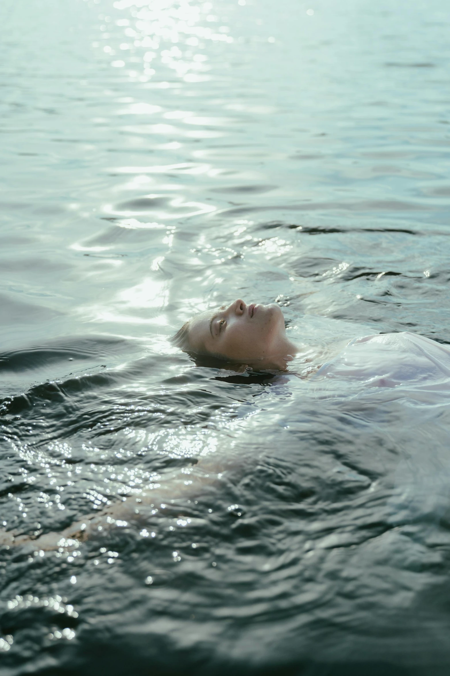 a woman floating on top of a body of water, face in water, lying down, subsurface scandering, light water