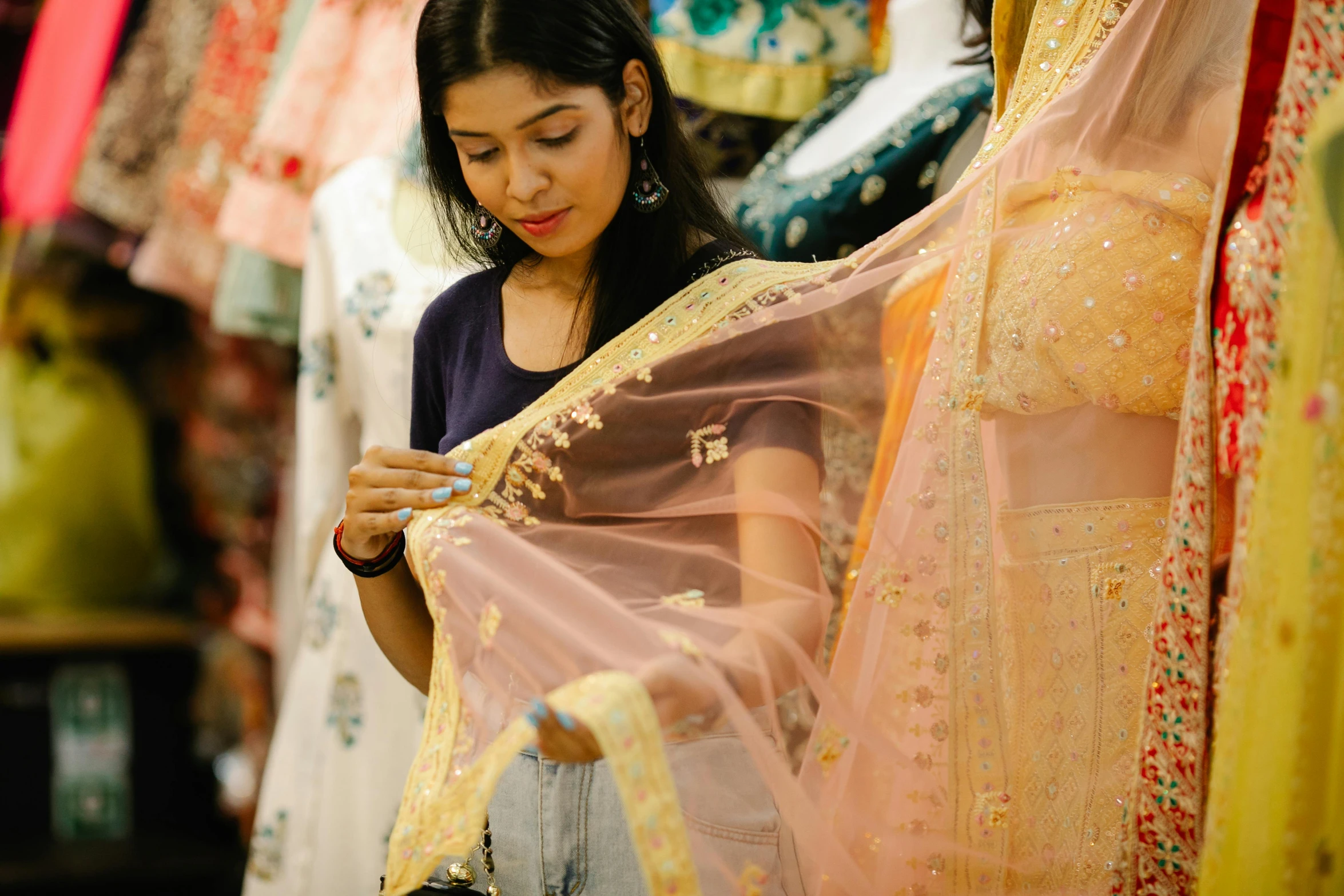 a woman standing in front of a rack of clothes, wearing a sari, look at the details, at a mall, wearing translucent sheet