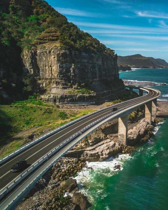 a train traveling over a bridge over a body of water, inspired by Sydney Carline, pexels contest winner, coastal cliffs, cars on the road, bulli, flat roads