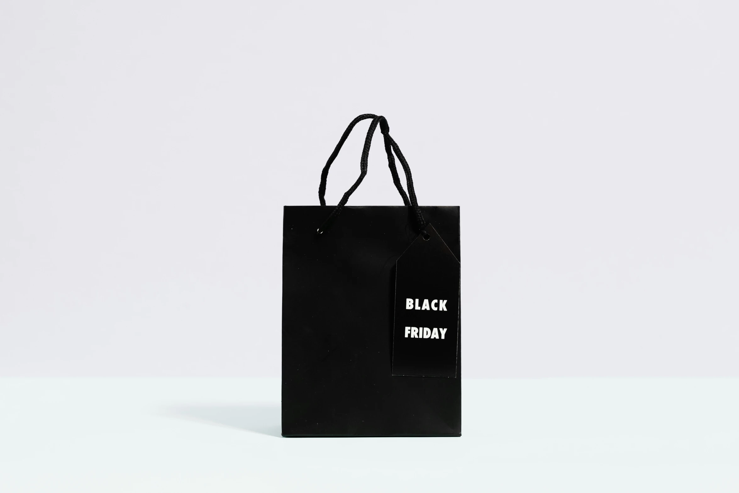 a black shopping bag sitting on top of a table, tumblr, hurufiyya, matte white background, main colour - black, holiday, tag