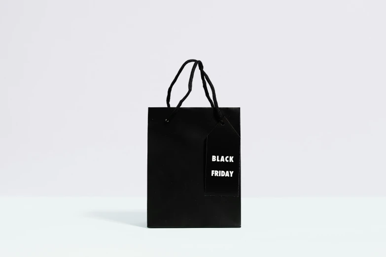 a black shopping bag sitting on top of a table, tumblr, hurufiyya, matte white background, main colour - black, holiday, tag