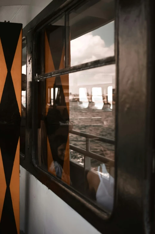 a man standing next to a window on a train, a picture, unsplash, graffiti, black and orange colour palette, reflections on the river, ship interior, close - up of the faces