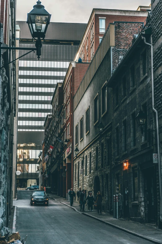 a car driving down a street next to tall buildings, inspired by Elsa Bleda, pexels contest winner, renaissance, back alley, quebec, people walking around, in a massive cavernous iron city