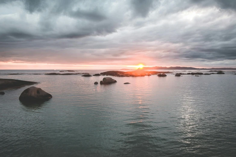 a body of water surrounded by rocks under a cloudy sky, setting sun, hamar, distant photo