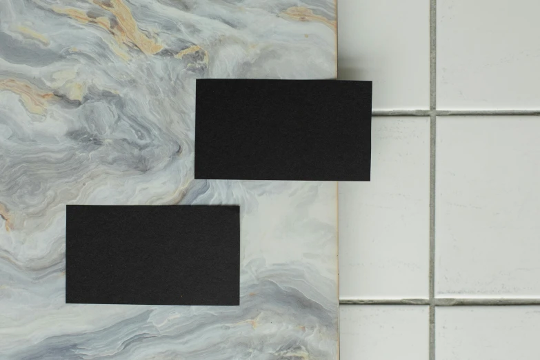 a couple of black squares sitting on top of a counter, inspired by Brice Marden, unsplash, handcrafted paper background, pair of keycards on table, main colour - black, granite