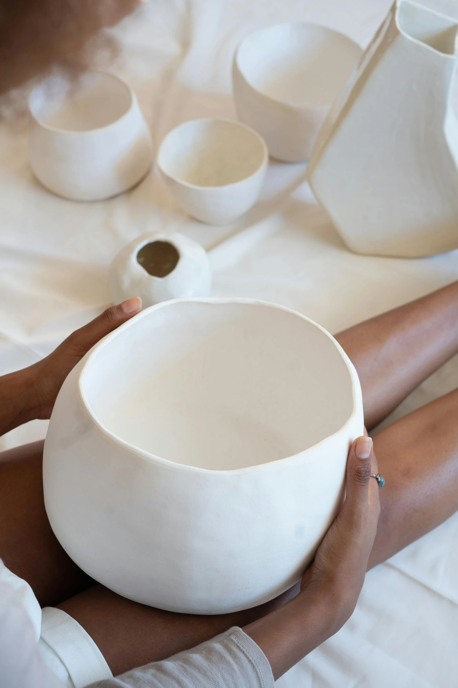 a woman sitting on a bed holding a white bowl, a marble sculpture, trending on unsplash, process art, bongos, made of clay, various sizes, head down