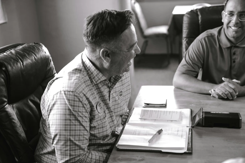 a black and white photo of two men sitting at a table, unsplash, teaching, timothy rees, person in foreground, register