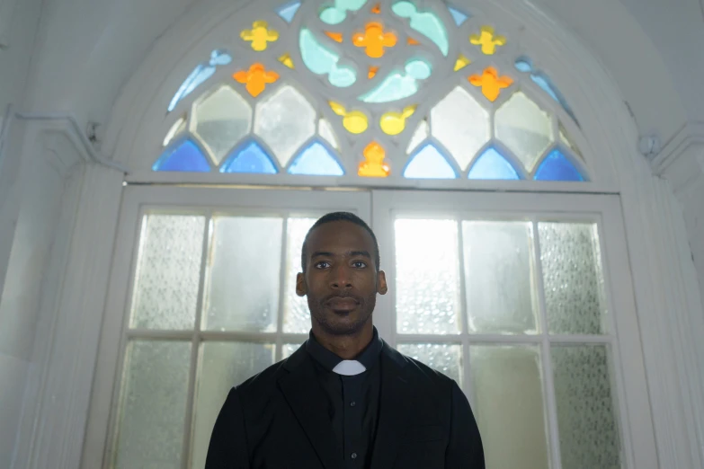 a man standing in front of a stained glass window, black main color, churches, front facing the camera, portrait image