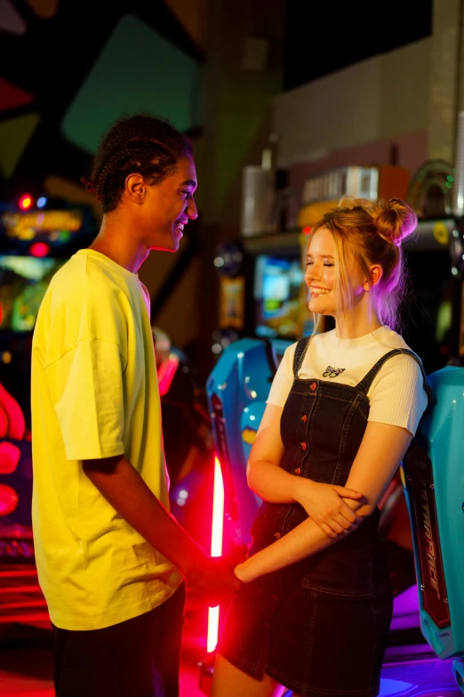 a couple of people standing next to each other, by John Luke, pexels, happening, arcade cabinet in background, sadie sink, summer evening, dreamworld