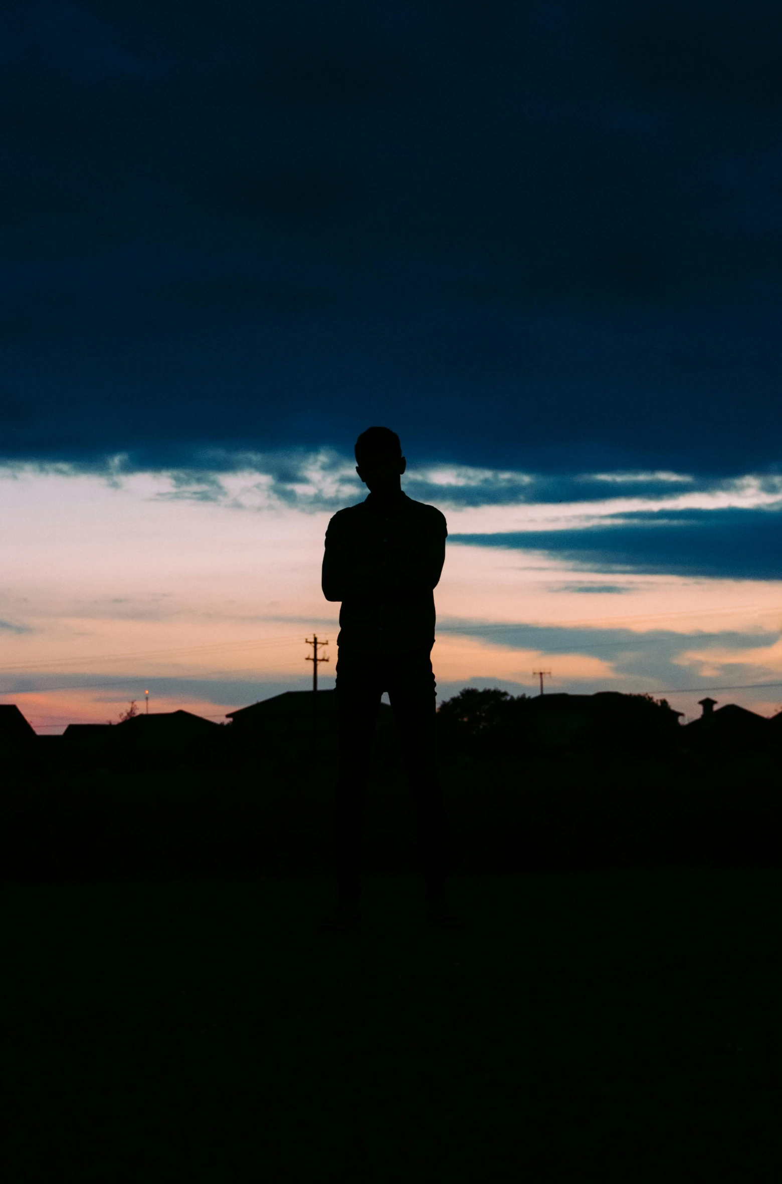 a man standing on top of a grass covered field, a picture, unsplash, silhouette :7, teenage boy, dusk sky, standing in street