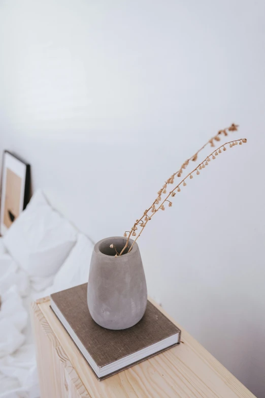 a vase sitting on top of a wooden table next to a bed, trending on pexels, with stars, sparse detail, detailed product image, smooth concrete