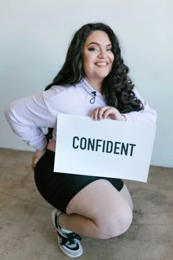a woman kneeling down holding a sign that says confident, featured on reddit, bbw, wearing tight simple clothes, profile image, bralette