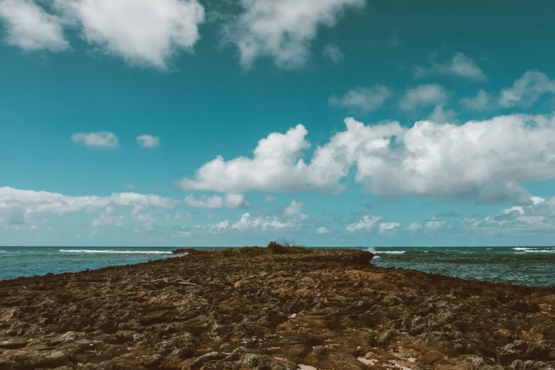 a small island in the middle of the ocean, unsplash, les nabis, rocky ground with a dirt path, under blue clouds, low quality photo, hd footage