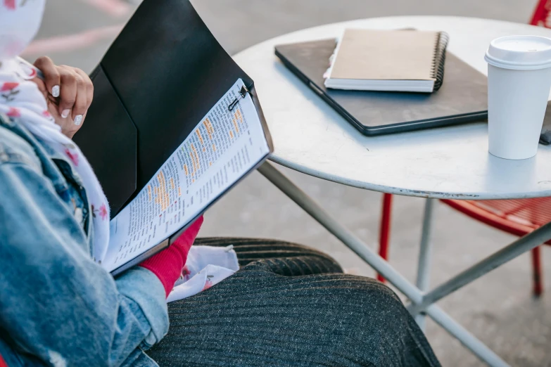 a woman sitting at a table reading a book, by Carey Morris, trending on unsplash, wizard reading a directory, cafe tables, idealised, close - up photo