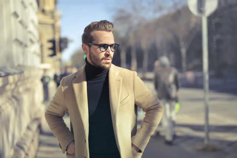 a man standing on a sidewalk with his hands in his pockets, pexels contest winner, wearing a turtleneck and jacket, wearing gold glasses, blond brown stubble thin beard, instagram post