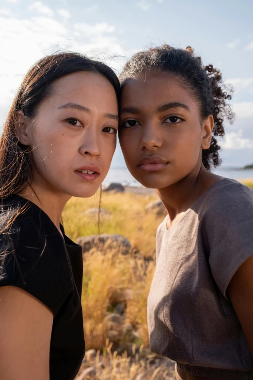 two women standing next to each other in a field, light-brown skin, perfectly lit. movie still, coastline, ying and yang