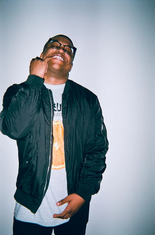 a man in a black jacket talking on a cell phone, an album cover, inspired by Greg Staples, unsplash, thick glasses, rubenesque, large black smile, looking to his side