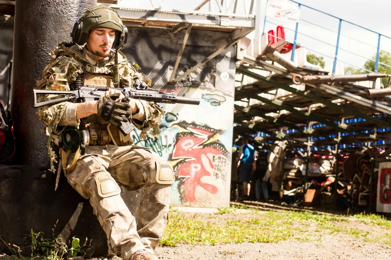 a man that is sitting down with a gun, by Adam Marczyński, reddit, paintball world cup, scene from live action movie, military base, advertising photo