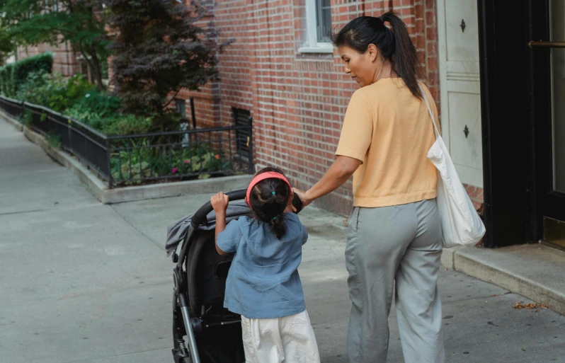 a woman pushing a child in a stroller, pexels contest winner, happening, standing with her back to us, neighborhood, brown, asian female