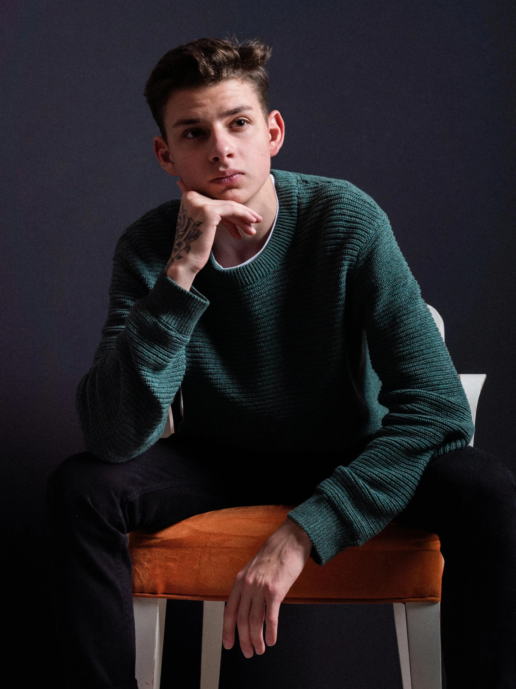 a man sitting on top of a wooden chair, inspired by Elsa Bleda, trending on unsplash, realism, wearing a green sweater, declan mckenna, frontal pose, thin young male