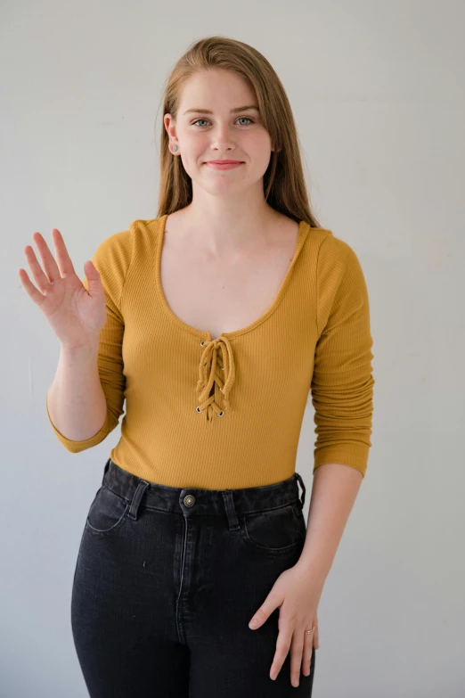 a woman standing in front of a white wall, an album cover, by Ellen Gallagher, shutterstock contest winner, renaissance, wearing yellow croptop, muted colored bodysuit, brown shirt, hr ginger