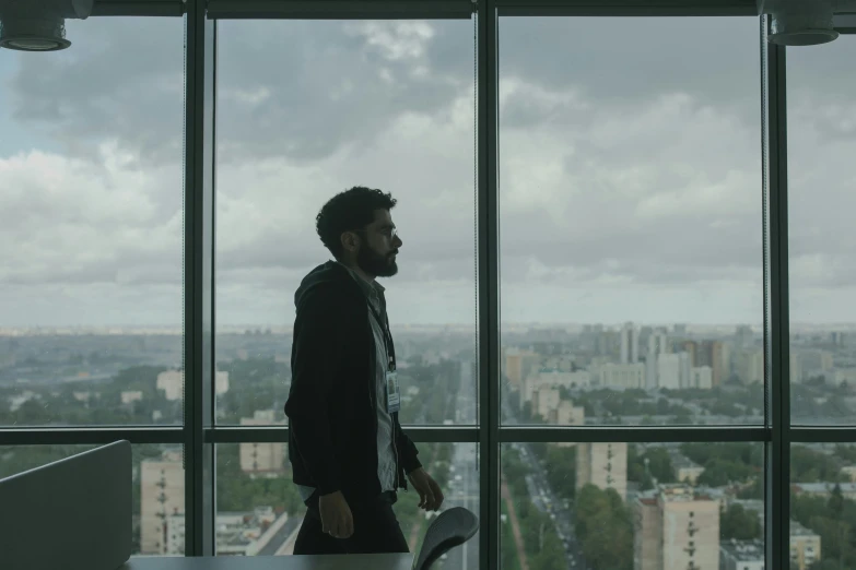 a man standing in front of a large window, movie still 8 k, h3h3, sat in an office, gloomy skies