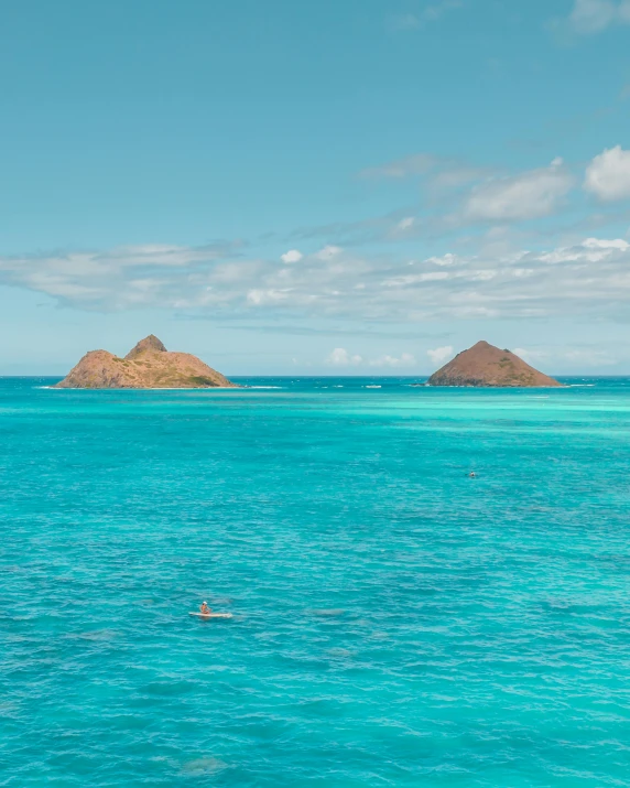 a couple of people swimming in the ocean, two medium sized islands, light blue water, lynn skordal, breathtaking colors