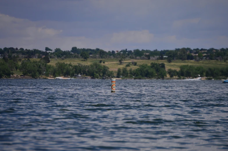 a man riding a surfboard on top of a body of water, view from the lake, from a distance, colour photo, vannessa ives