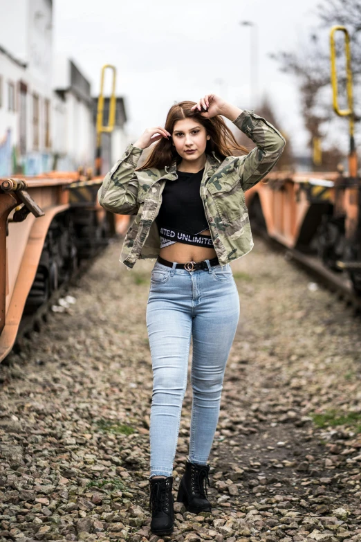 a woman standing in front of a train, by Niko Henrichon, pexels contest winner, wearing camo, wearing jeans, 2 4 year old female model, wearing crop top