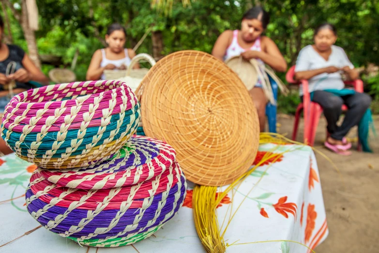 a group of people sitting around a table with baskets on it, colourful, puerto rico, swirling, indigenous