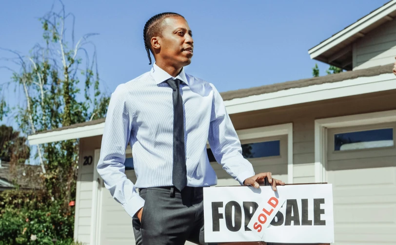 a man holding a for sale sign in front of a house, pexels contest winner, realism, ( ( dark skin ) ), looking to his side, wearing a suit, charts