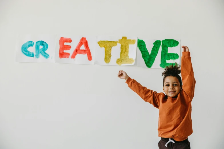 a little boy holding up a sign that says creative, pexels contest winner, coloured photo, thumbnail, trending artstaition, flatlay