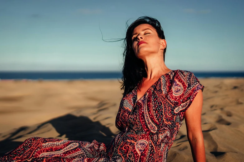 a woman sitting on top of a sandy beach, a portrait, pexels contest winner, arabesque, sunbathed skin, wearing in a summer dress, feeling good, patterned clothing