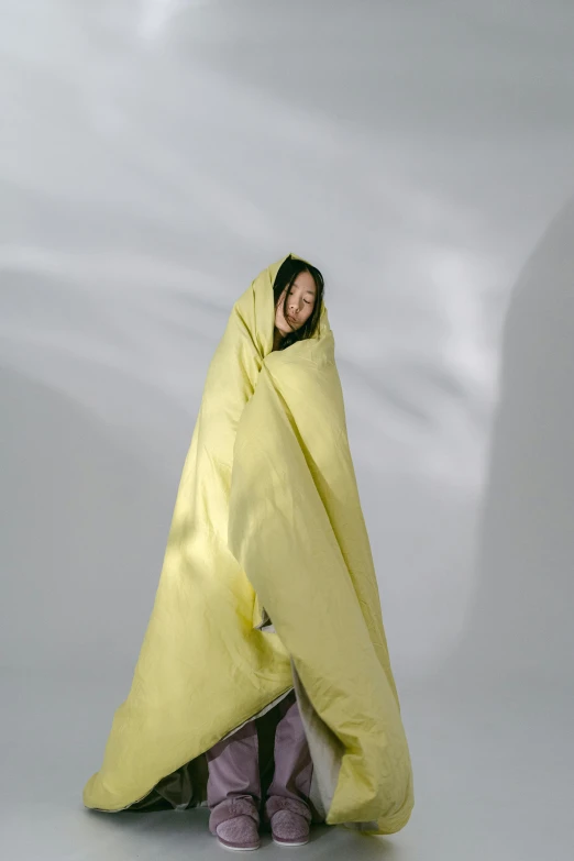 a woman wrapped up in a yellow blanket, by Fei Danxu, happening, light mode, lined in cotton, excitement, plain background