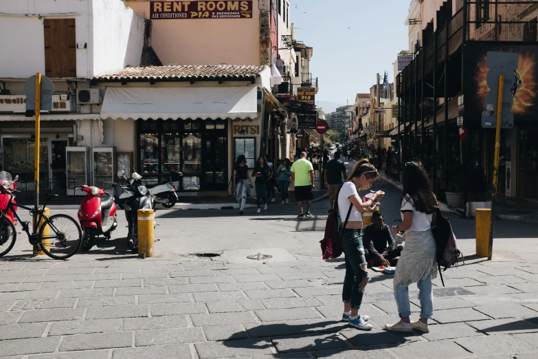 a group of people walking down a street, meni chatzipanagiotou, jenna barton, sunny day time, street - level