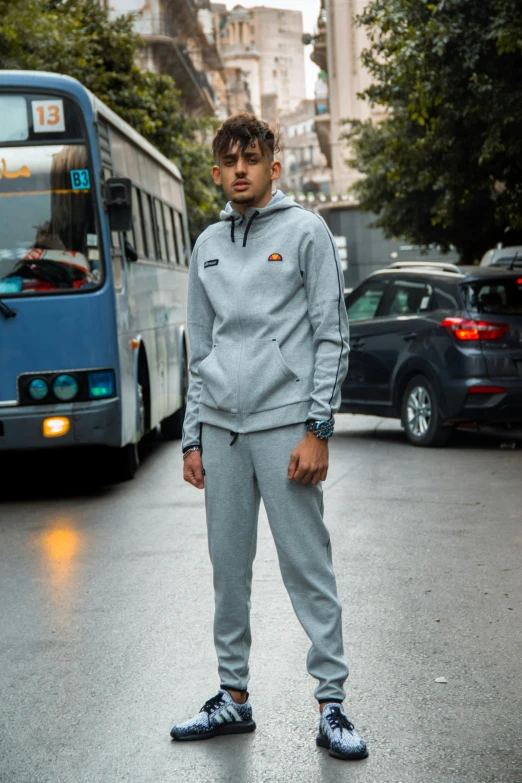 a man standing on the street in front of a bus, inspired by Ugo Nespolo, instagram, renaissance, wearing a track suit, flat grey color, technical suit, roma