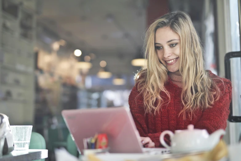 a woman sitting at a table with a laptop, pexels contest winner, happening, wearing a red turtleneck sweater, a girl with blonde hair, happy girl, people at work