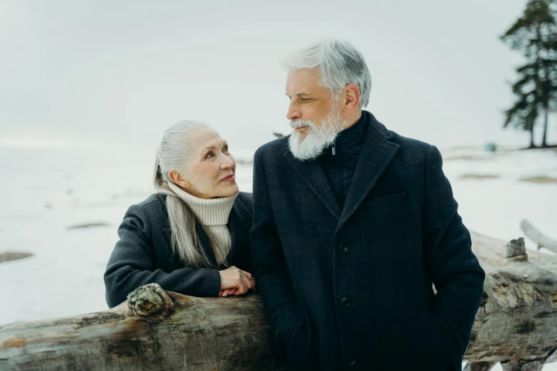 a man and a woman standing next to each other, pexels contest winner, gray beard, winter setting, coastal, looking left