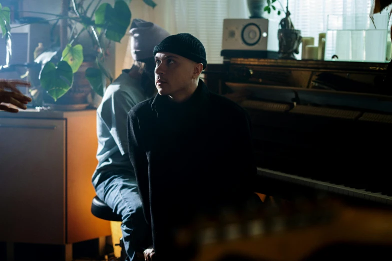 a man standing next to a piano in a living room, an album cover, unsplash, realism, with black beanie on head, two buddies sitting in a room, official music video, billy corgan