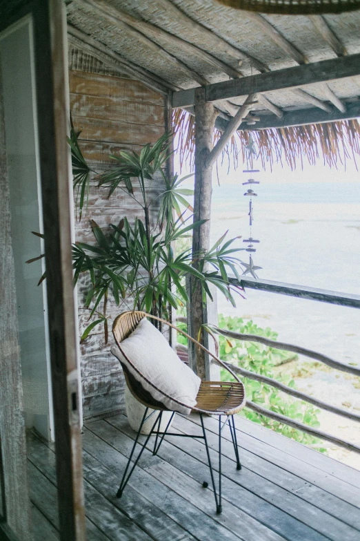 a chair sitting on top of a wooden porch, bamboo huts, full room view, seaview, next to a plant