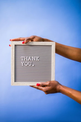 a woman holding a sign that says thank you, an album cover, trending on unsplash, square pictureframes, pale blue backlight, sustainable materials, high quality photo