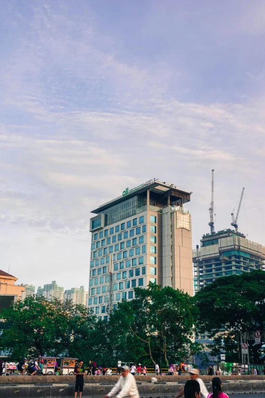 a group of people riding bikes down a street, a screenshot, inspired by Cheng Jiasui, unsplash, happening, colombo sri lanka cityscape, hotel room, building facing, bright sky