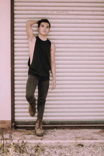 a man standing in front of a garage door, an album cover, by Robbie Trevino, trending on pexels, wearing a camisole and boots, julian ope, man standing in defensive pose, androgynous person