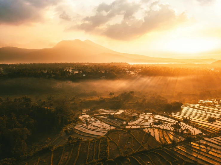 an aerial view of a farm with mountains in the background, pexels contest winner, sumatraism, golden hour sun rays, golden hour in boracay, grey, golden hues