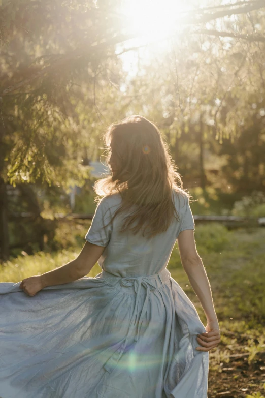 a woman in a blue dress walking through a field, looking off into the sunset, walking through the trees, outside, 2019 trending photo