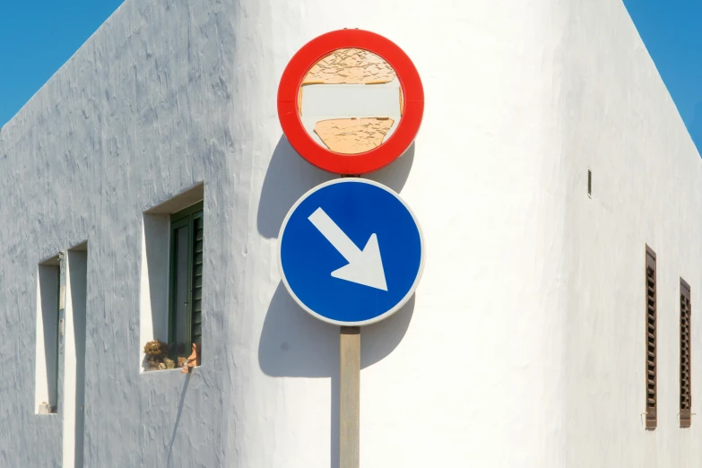 a close up of a street sign with a building in the background, inspired by Julio Larraz, unsplash, postminimalism, ibiza, rounded shapes, with two arrows, white and blue