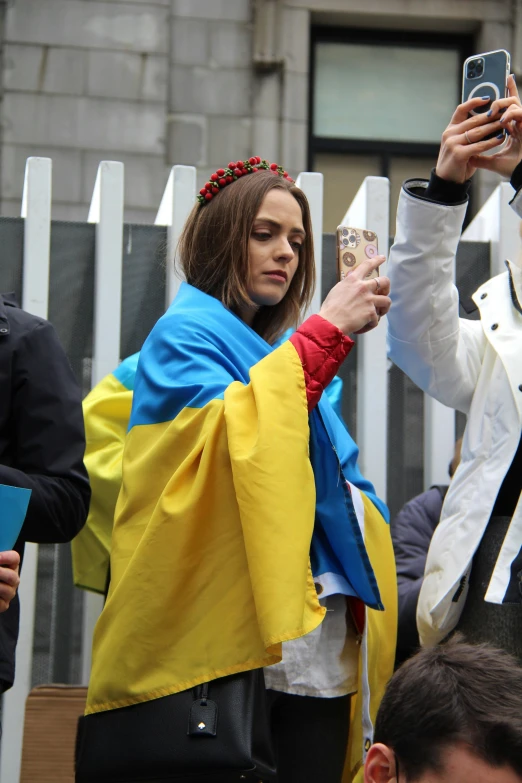 a group of people taking pictures with their cell phones, antipodeans, ukrainian flag on the left side, bright red cape on her back, emily blunt, wikimedia commons